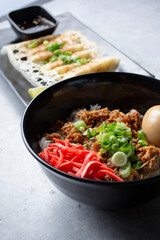 A closeup view of a garlic pork bowl, with a plate of gyoza.