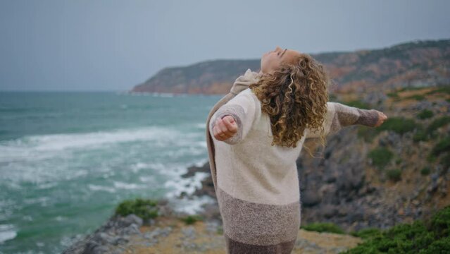 Lady spending sea vacation on cloudy rocky shore closeup. Carefree woman raising