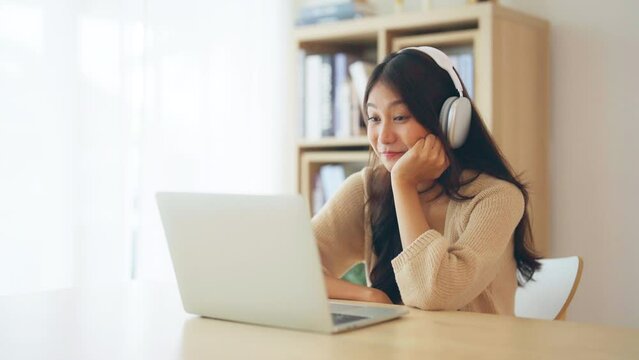 Young asian woman wearing headset while working on computer laptop at house. Work at home, Video conference, Video call, Student learning online class