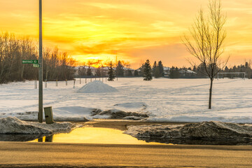 Orange color sunset reflection on puddle from melted snow at the edge of sidewalk in mwltdoqn spring seasow