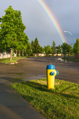 Yellow and blue color fire hydrant at city wet street after rain and rainbow