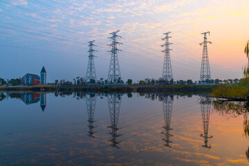 In the evening, the high-voltage power tower stands tall and spectacular in the park on the outskirts of the city - obrazy, fototapety, plakaty