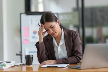 Asian businesswoman who is tired has a headache, is stressed, sleepy, angry, and bored from sitting...