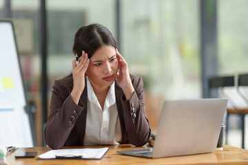Asian businesswoman who is tired has a headache, is stressed, sleepy, angry, and bored from sitting at a desk for a long time doing contact work. online business on laptop Office syndrome concept.