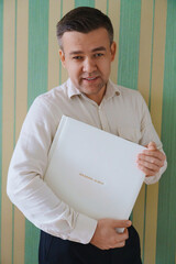 A man holds a photo book in a white leather cover 