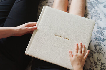 The hands are holding a wedding book in a white leather cover 