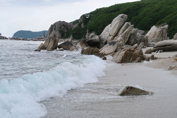 sea blue waves at windy day on the beach, white foam and splash, stones on the shore, porous rocks,...