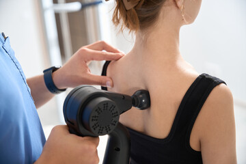 Physiotherapist massages patients back with special massager