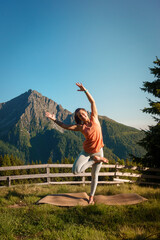 Yoga Pose Baum Variation - Sportliche Frau in Leggings und orangefarbenem Top macht Yoga mit Blick...