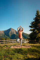 Yoga Pose Baum Variation - Sportliche Frau in Leggings und orangefarbenem Top macht Yoga mit Blick...