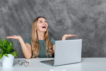 Gorgeous female model with blond hair in gray dress posing with a laptop near green flower