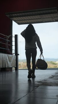 Female Muay Thai boxer walking with gym bag in club.