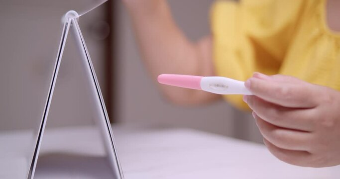 Expectant mother going through a calendar to count the weeks to her expected due date while holding a pink pregnancy test kit on her left hand.