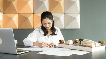 Portrait of beautiful young architect engineer measures house model while taking a note on...
