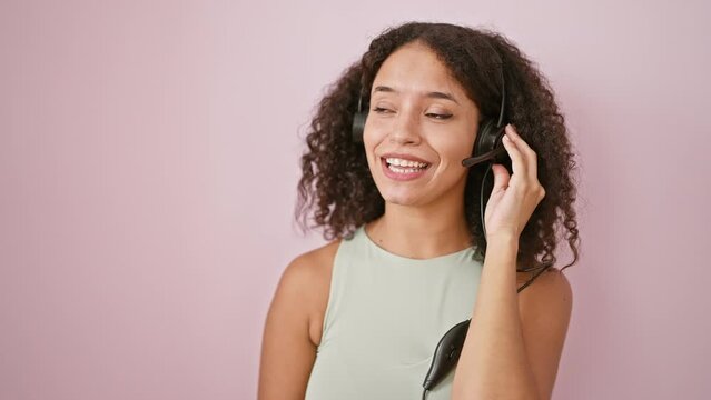 Confident young hispanic woman boss enjoying aid work, smiling as she speaks over headset, isolated on pink. successful, beautiful manager wearing work headset. happy business professional.