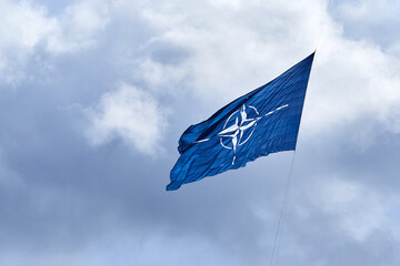 NATO flag on cloudy sky. Flying in the sky - obrazy, fototapety, plakaty