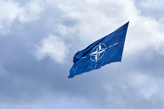Fototapeta NATO flag on cloudy sky. Flying in the sky