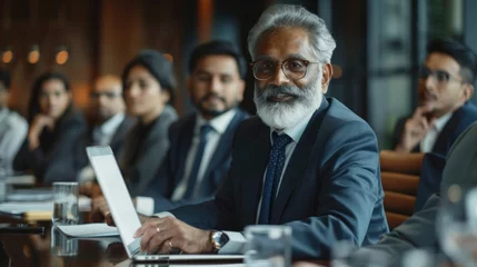 Muurstickers Successful Indian CEO Making a Presentation on a Laptop to a Board of Directors During a Corporate Meeting. South Asian Business Partners Discussing International Markets © 2D_Jungle