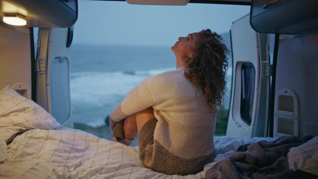 Dreamy traveller sitting camping van looking on evening seascape. Happy woman