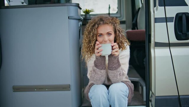 Curly woman drinking cappuccino sitting trailer stairs. Happy lady enjoy coffee