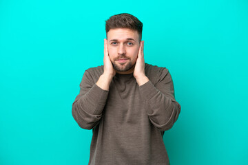 Young caucasian man isolated on blue background frustrated and covering ears