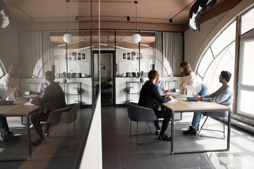 Young business project leader woman talking to diverse team at meeting, giving creative ideas, plan, marketing strategy for startup, standing, leaning on table. Full length shot with reflection