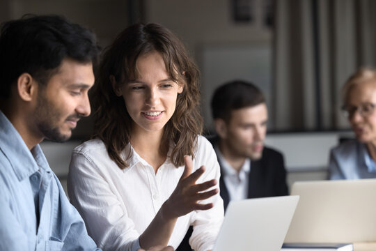 Multiethnic couple of positive colleagues talking at laptop, working together in co-working space, discussing creative ideas for project, watching online video presentation - Powered by Adobe