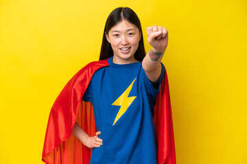 Young Chinese woman isolated on yellow background in superhero costume with proud gesture