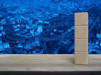 Four wood block cubes on wooden table over modern city tower, street, expressway and skyscraper