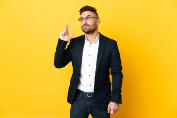 Businessman over isolated yellow background with fingers crossing and wishing the best