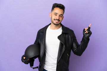 Young man with a motorcycle helmet isolated on purple background showing and lifting a finger in...