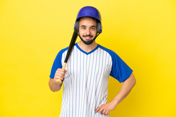 Young caucasian man playing baseball isolated on yellow background posing with arms at hip and smiling