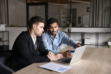 Serious multiethnic business colleagues working on job tasks together, talking at workplace table,...