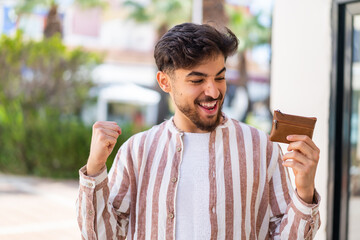 Handsome Arab man holding a wallet at outdoors celebrating a victory
