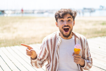 Handsome Arab man with a cornet ice cream at outdoors surprised and pointing finger to the side