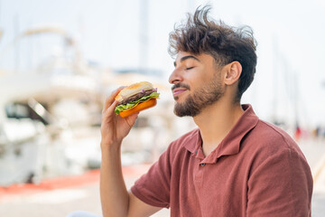 Young Arabian handsome man at outdoors holding a burger