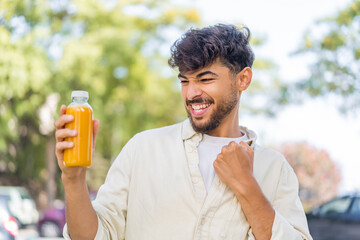 Young Arabian handsome man holding an orange juice at outdoors celebrating a victory
