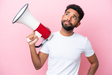 Young Brazilian man isolated on pink background holding a megaphone and thinking