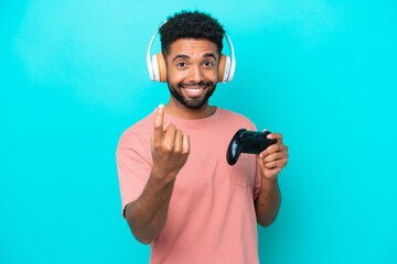 Young brazilian man playing with a video game controller isolated on blue background doing coming...