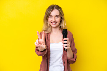 Young singer caucasian woman picking up a microphone isolated on yellow background smiling and...