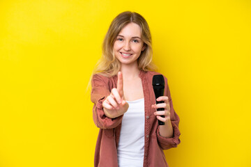 Young singer caucasian woman picking up a microphone isolated on yellow background showing and...
