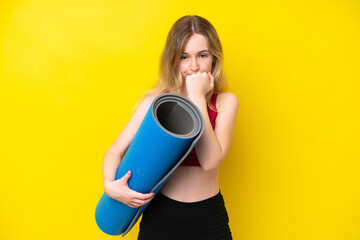 Young sport caucasian woman going to yoga classes while holding a mat isolated on yellow background...