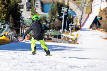 skier boy in a green helmet descends from the mountain in carving style. Family active recreation