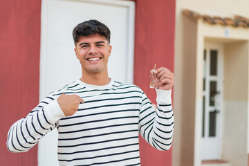 Young hispanic man holding home keys at outdoors with surprise facial expression