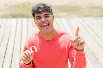 Young hispanic man holding invisible braces at outdoors pointing up a great idea