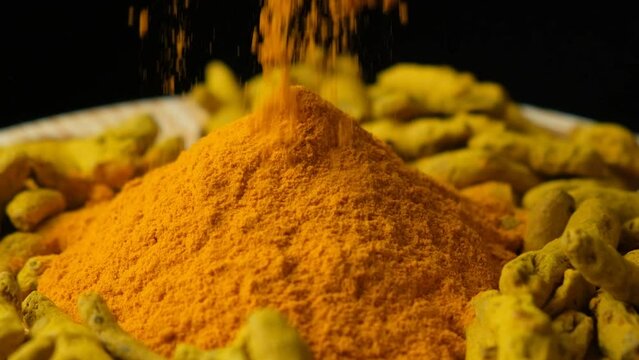 Turmeric powder sprinkled on wooden dish with powder and dry turmeric root, slow motion.