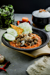 Hot plate Shell or Sambal Gami Kerang is Traditional food from Indonesia. Served on plate with a bowl of rice and vegetables top view. Super hot and spicy food