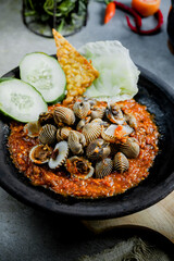 Hot plate Shell or Sambal Gami Kerang is Traditional food from Indonesia. Served on plate with a bowl of rice and vegetables top view. Super hot and spicy food