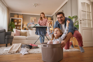Little girl and dad laughing while playing with the laundry basket in living room