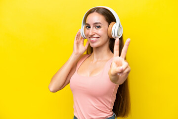 Young caucasian woman isolated on yellow background listening music and singing